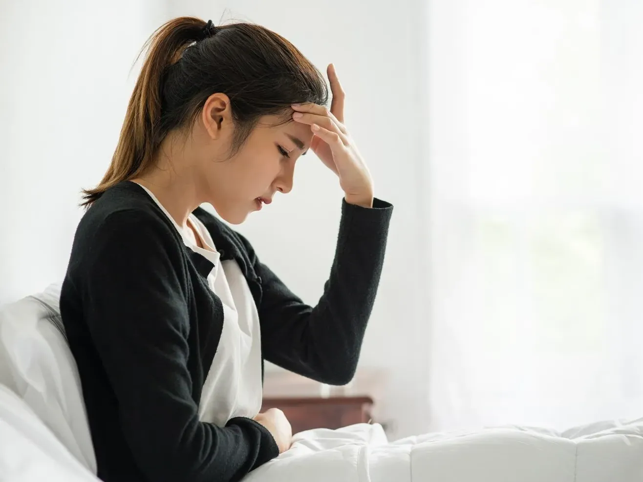 Woman sitting on the edge of her bed holding her head during a headache