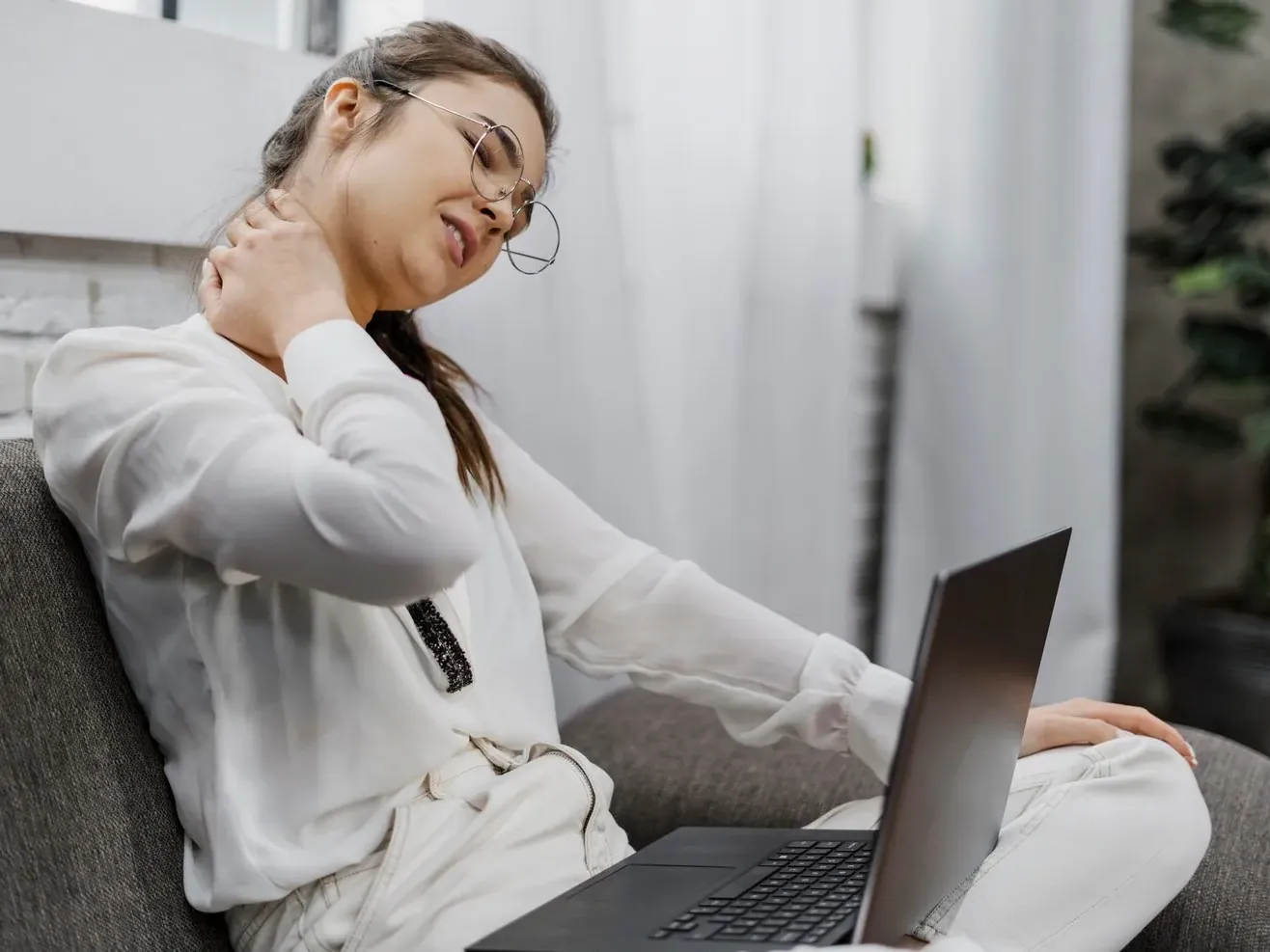 Woman at a laptop reaching back for her stiff neck